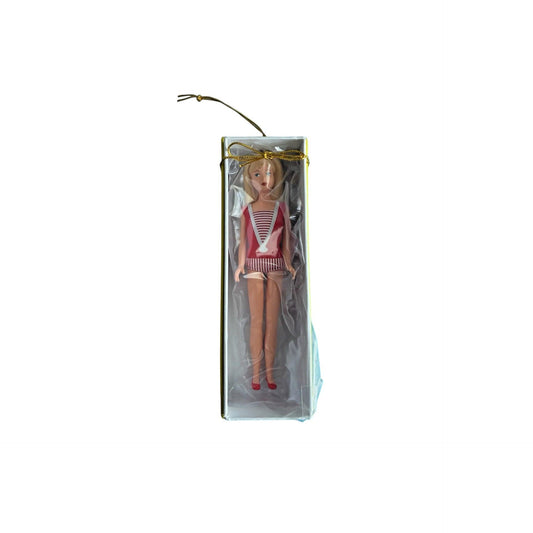 Barbie doll in a red and white striped swimsuit with a gold bow in her hair, packaged in clear plastic on a white background.