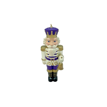 Nutcracker figurine with purple outfit and gold accents on a white background
